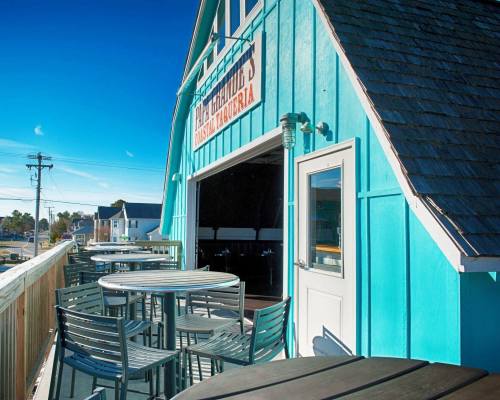A bright blue building with outdoor seating and tables, overlooking a sunny landscape.
