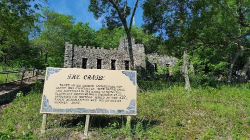 A stone structure resembling a castle, surrounded by trees, with a sign describing its historical significance.