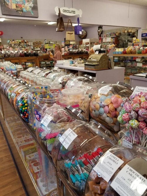 A colorful candy shop display featuring jars of various sweets, chocolates, and treats along a glass counter.