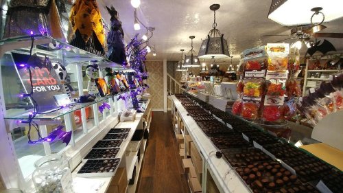 A cozy candy shop filled with colorful treats, chocolates, and Halloween decorations, illuminated by warm lights.
