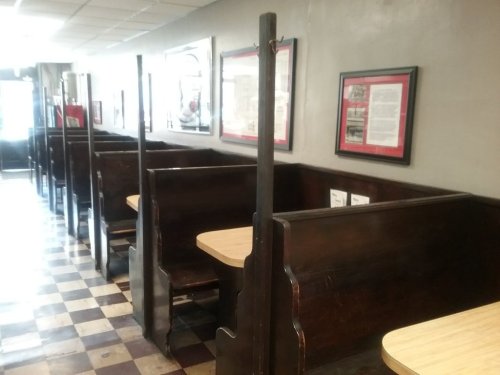 A row of wooden booths with tables in a diner, featuring a checkered floor and framed pictures on the walls.