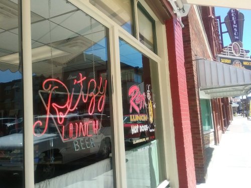 Neon sign for "Ritzy Lunch" and "Beer" in a window, with a street view of a theater in the background.