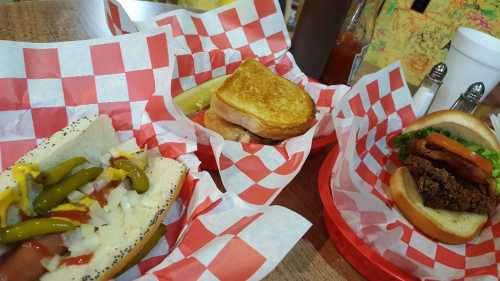 Three sandwiches on red and white checkered paper: a hot dog with toppings, a grilled cheese, and a burger with toppings.