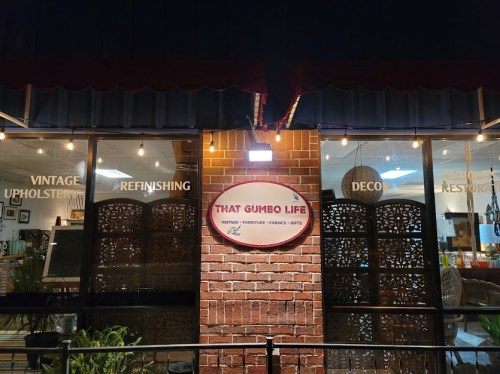 Sign for "That Gumbo Life" storefront, featuring vintage decor and upholstery services, with warm lighting and a welcoming vibe.
