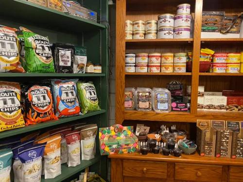 A display of various snacks, including chips and candies, on shelves and in jars, in a cozy store setting.