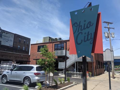 Sign for "Ohio City" in front of a modern brick building with outdoor seating and a clear blue sky.