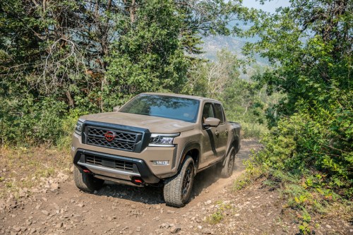A rugged truck driving on a dirt path through a forested area, surrounded by trees and greenery.
