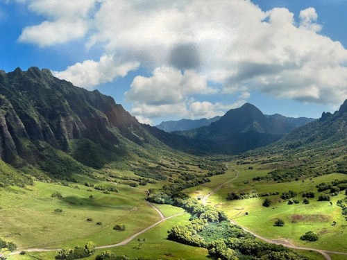 A lush green valley surrounded by mountains under a partly cloudy sky.