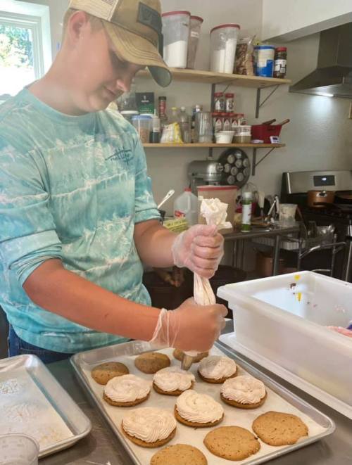 A person in a blue tie-dye shirt decorates cookies with frosting in a kitchen.