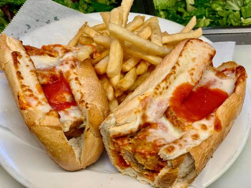 Two meatball subs topped with marinara sauce and melted cheese, served with a side of crispy French fries.