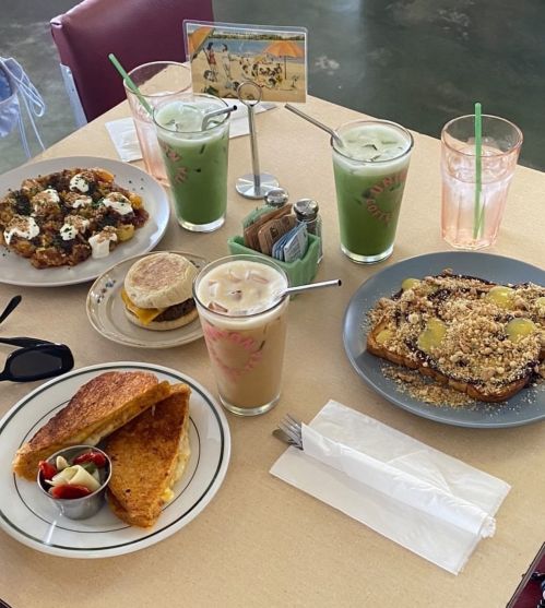 A table set with various dishes: a sandwich, French toast, a breakfast platter, and drinks in glasses.