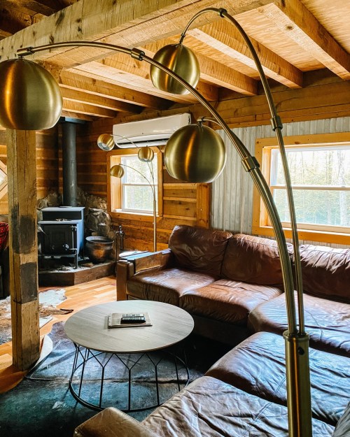 Cozy living room with a brown leather sofa, a round coffee table, and a stylish arc floor lamp in a rustic cabin setting.