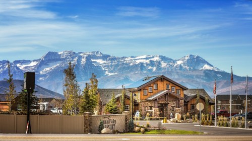 A rustic lodge surrounded by mountains, with clear blue skies and greenery in the foreground.