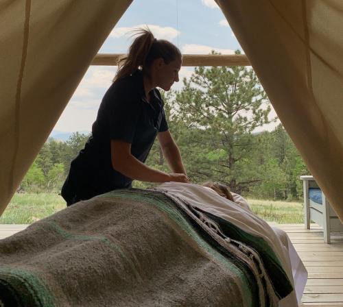 A person giving a massage to someone lying on a table, surrounded by nature in a tent-like setting.