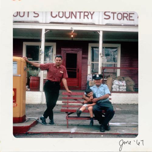 Two men and a boy sit on a bench outside a country store, with a vintage gas pump nearby. Date: June '67.