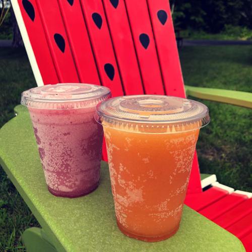 Two colorful smoothies, one purple and one orange, sit on a bright green chair with a red watermelon-patterned background.