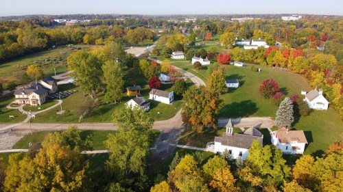 Aerial view of a colorful autumn landscape featuring small houses and trees with vibrant fall foliage.