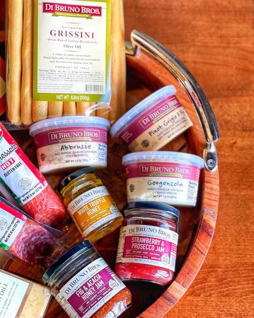 A wooden platter featuring various gourmet items, including grissini, cheeses, and jams from Di Bruno Bros.