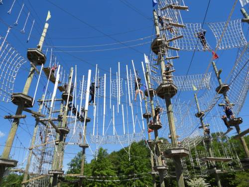 A high ropes course with participants navigating obstacles among wooden towers against a clear blue sky.