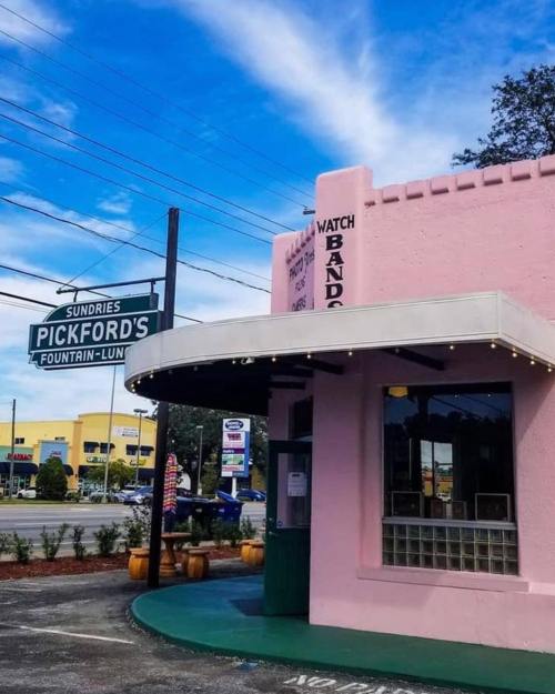 A pink building with a marquee sign reading "Pickford's Fountain-Lun" under a blue sky with scattered clouds.