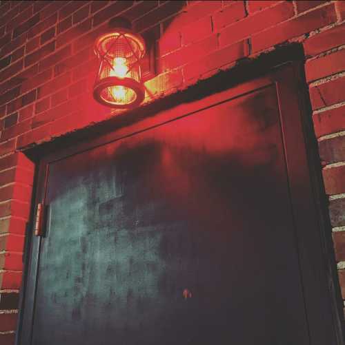 A dark door with a red lantern above it, set against a textured brick wall.