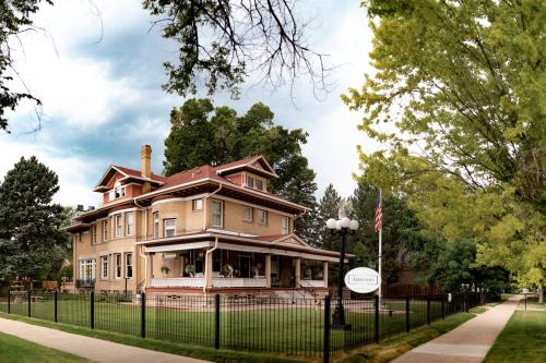 A large, historic house with a porch, surrounded by a green lawn and trees, located near a sidewalk and street.