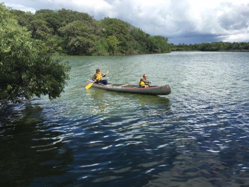 Two people in a canoe paddle on a calm lake surrounded by lush greenery under a cloudy sky.