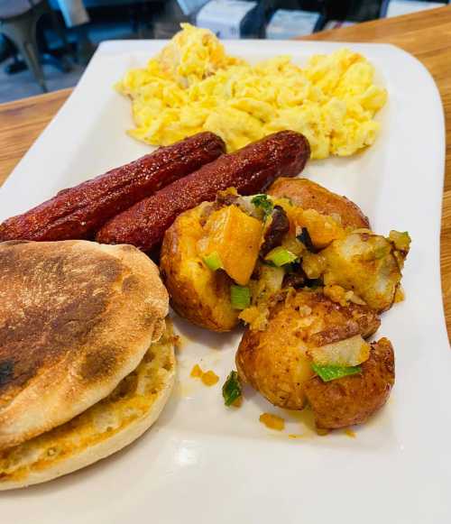 A plate of breakfast featuring scrambled eggs, sausage links, seasoned potatoes, and a toasted English muffin.