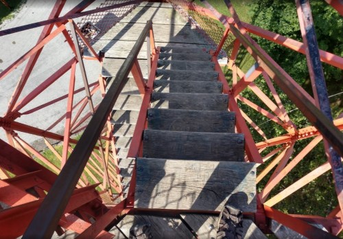 View from the top of a metal staircase, looking down at wooden steps and red metal framework.