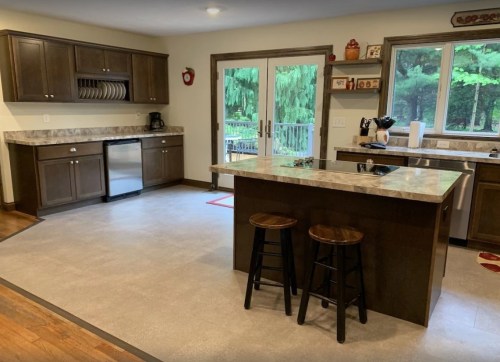 Modern kitchen with dark cabinets, a marble countertop island, and sliding glass doors leading to a green outdoor view.