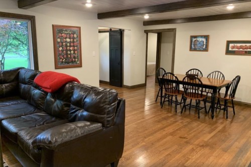 Cozy living space featuring a leather couch, dining table, and wooden floors, with artwork on the walls.