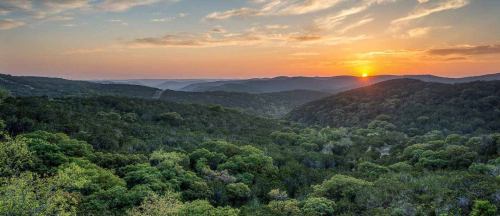 A scenic view of rolling hills and lush greenery at sunset, with warm colors illuminating the sky.