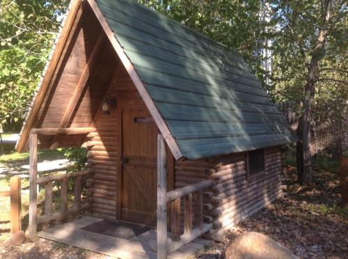 A small wooden cabin with a green roof, surrounded by trees and a stone pathway.