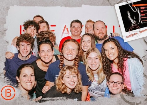 A group photo of smiling people posing together, with a mix of adults and teenagers in a casual setting.