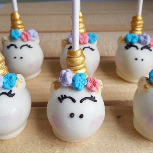 Five cute unicorn cake pops with colorful decorations and golden horns on a wooden surface.