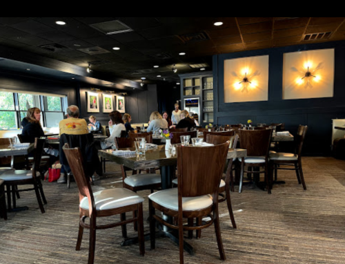 A cozy restaurant interior with wooden tables and chairs, featuring diners and soft lighting on the walls.
