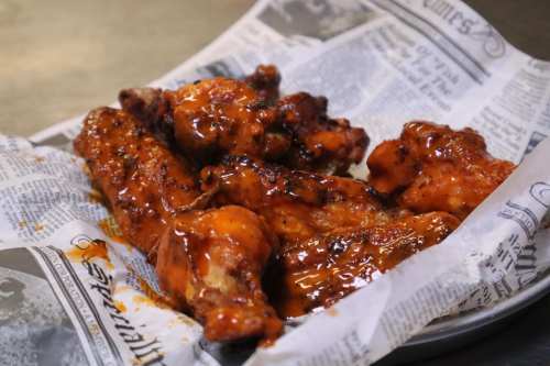 A plate of spicy, glazed chicken wings served on crumpled newspaper.