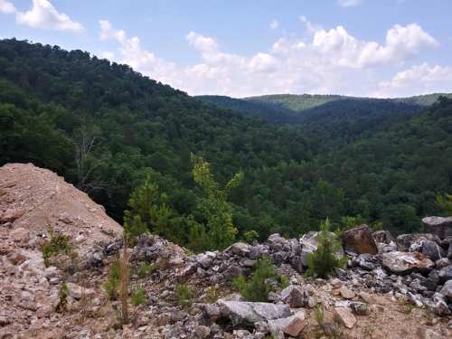 A scenic view of lush green mountains under a partly cloudy sky, with rocky terrain in the foreground.