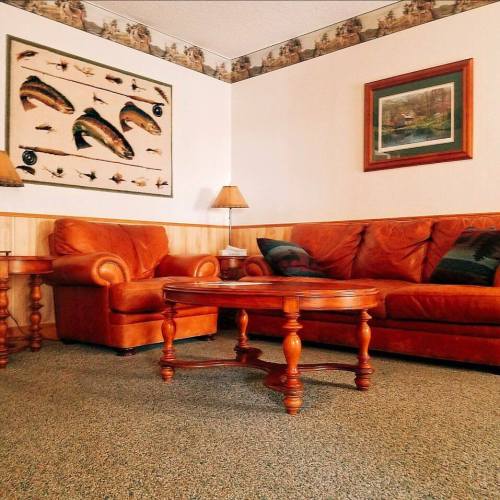 Cozy living room with orange leather sofas, a wooden coffee table, and fishing-themed decor on the walls.