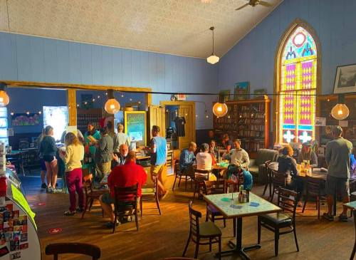 A cozy café with people socializing, colorful stained glass windows, and bookshelves in a warm, inviting atmosphere.
