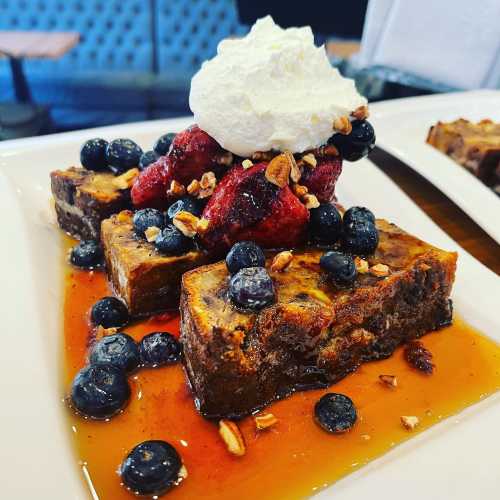 A dessert plate featuring chocolate cake topped with whipped cream, blueberries, strawberries, and granola.