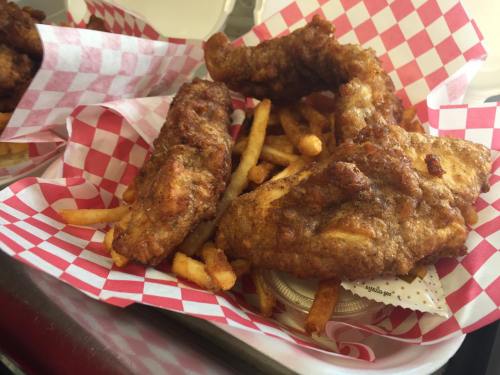 A basket of crispy fried chicken wings served with golden French fries, lined with red and white checkered paper.