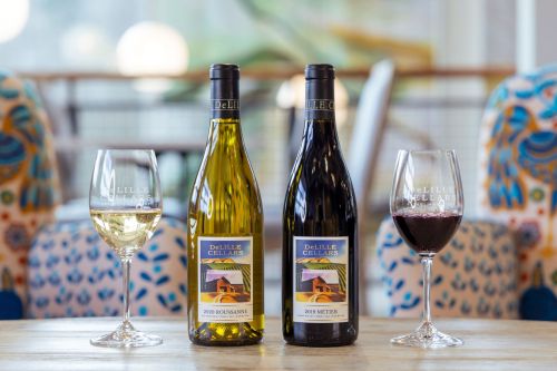 Two bottles of wine with glasses of white and red wine on a table, set in a cozy, colorful environment.