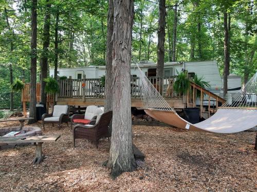 A cozy outdoor space with a hammock, seating area, and a mobile home surrounded by trees.