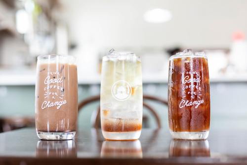 Three glasses of coffee drinks on a table: a chocolate drink, a clear iced drink, and a dark iced coffee.