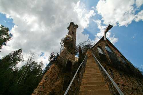 A unique stone tower with a spiral staircase, surrounded by trees and a dramatic sky filled with clouds.