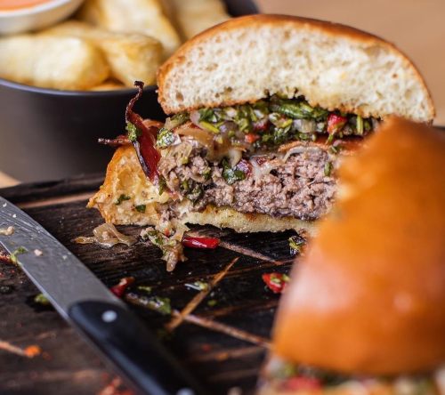 A close-up of a juicy burger with toppings, served on a wooden board alongside a bowl of fries.