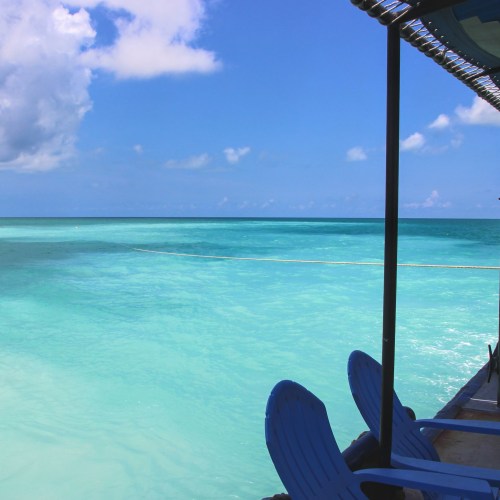 A serene view of turquoise waters under a blue sky, with lounge chairs by the shore.