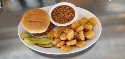A plate with a burger, pickles, fried corn nuggets, and a bowl of baked beans.