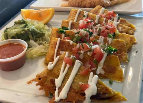 A plate of enchiladas topped with sour cream, tomatoes, and cilantro, served with guacamole, lettuce, and salsa.